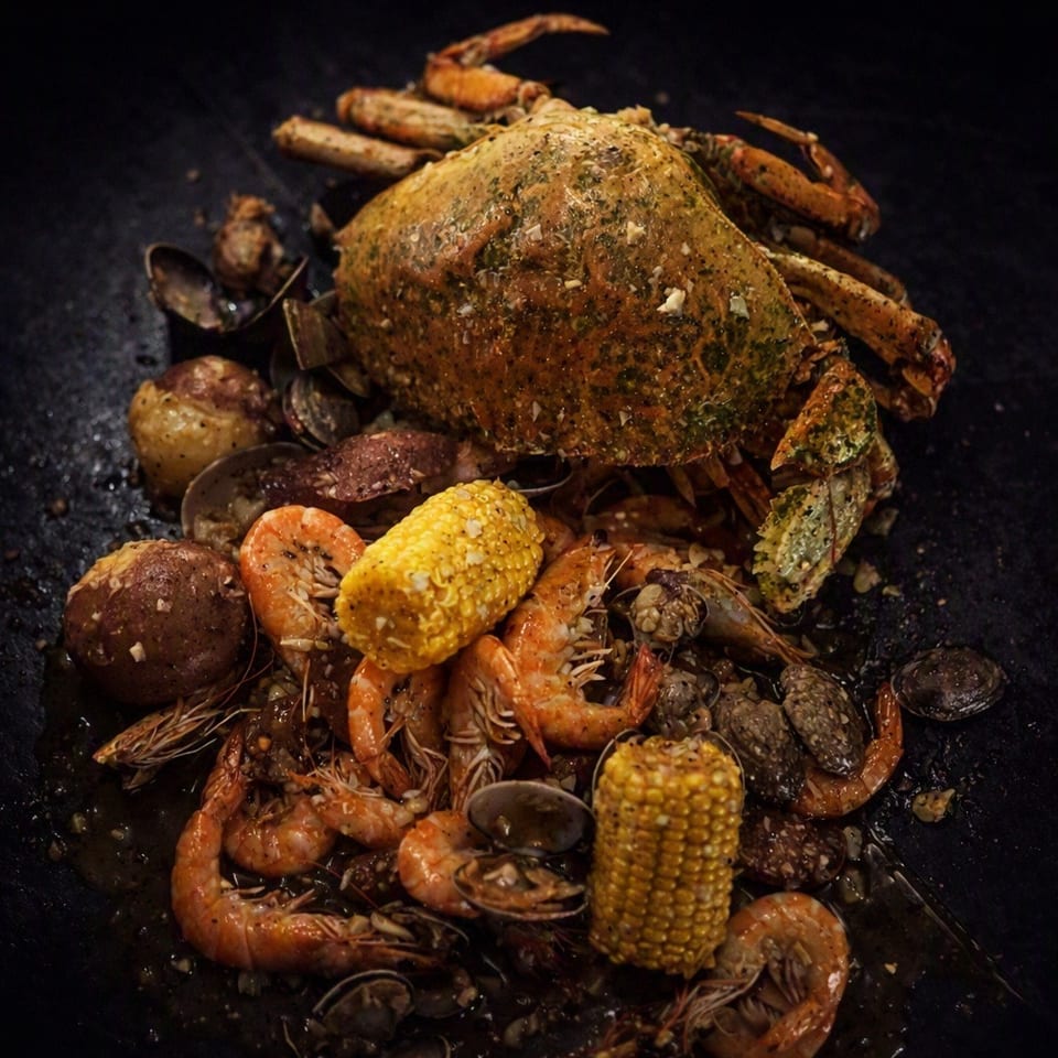 A seasoned seafood boil with a large crab, shrimp, clams, corn on the cob, and potatoes.