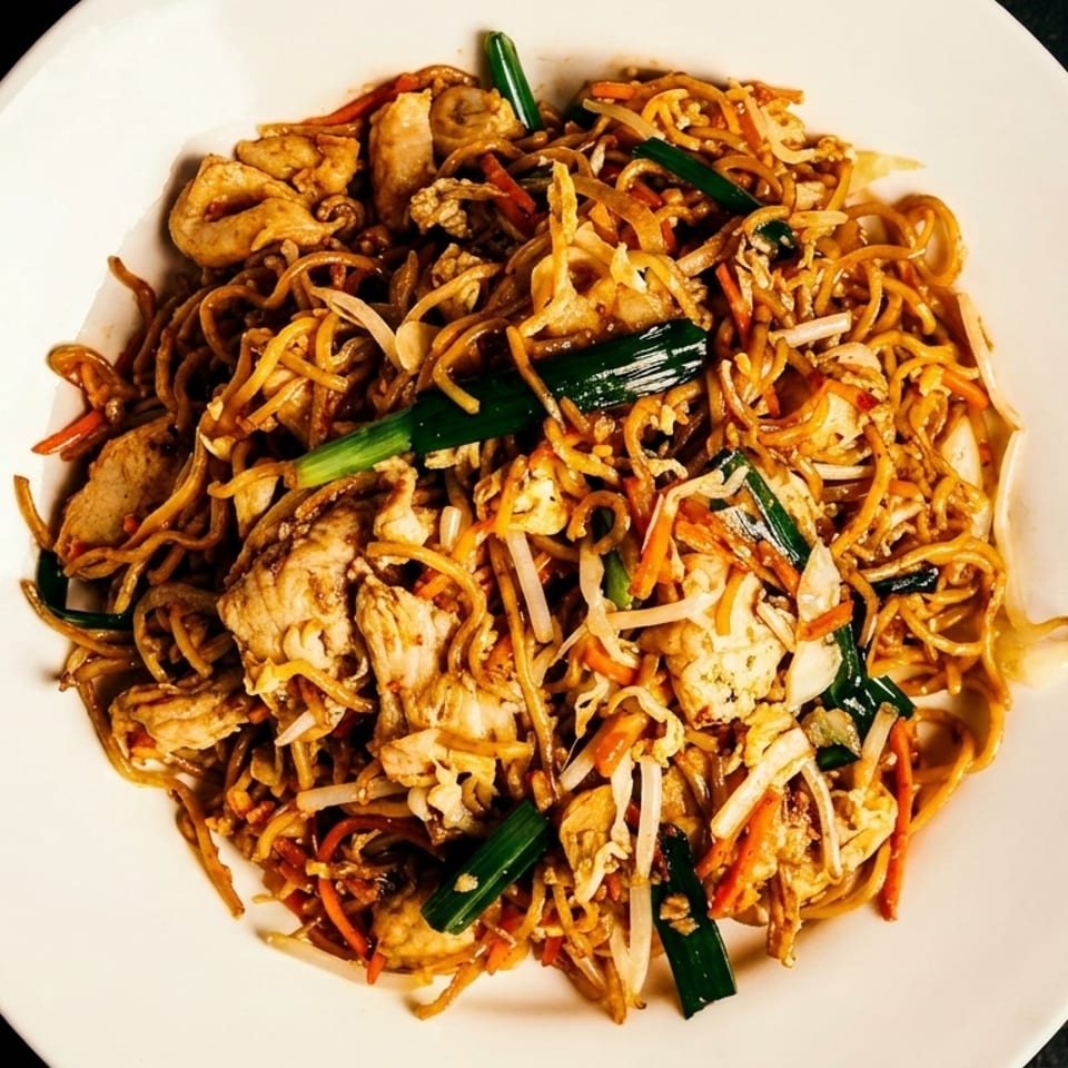 A white plate filled with chicken lo mein, featuring noodles, chicken, and vegetables.