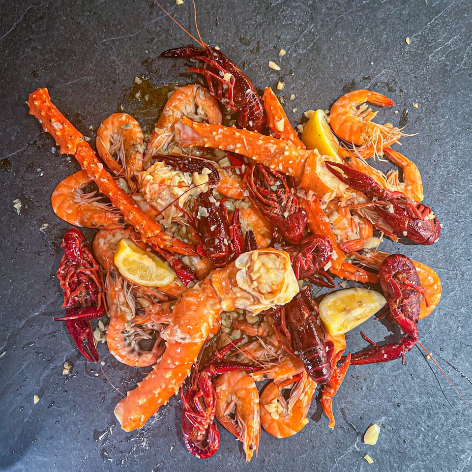 Seafood boil with shrimp, crawfish, crab legs, lemon, and garlic on a dark stone surface.